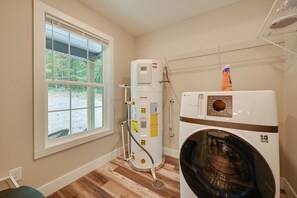 A laundry room with a front-loading washer and dryer, a water heater, and a window with blinds. - Home Near Kentucky Lake & Paris Landing! (Buchanan)