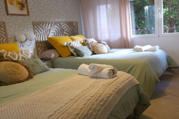 A hotel room with two beds, each with a different patterned bedspread, multiple pillows, and a window with curtains.