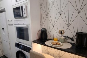 Eine kompakte Küche mit Mikrowelle, Ofen und Kaffeemaschine auf der Arbeitsplatte, sowie eine Wand mit geometrischem Muster.