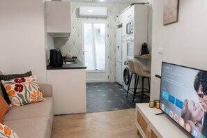 A compact living space with a kitchenette, a sofa with floral cushions, and a television displaying a movie.
