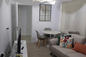 Ein Wohnzimmer mit einer Couch, einem Fernseher, einem Esstisch mit Stühlen und einem Fenster mit Blick.