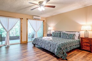 A bedroom with a bed, curtains, a ceiling fan, an air conditioning unit, and a nightstand with a lamp. - Hilltop Hideaway in Sapphire Near Lake Glenville (Sapphire)
