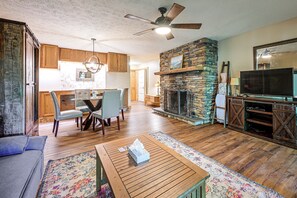 A spacious living area with a stone fireplace, a dining table with chairs, a television, and a ceiling fan. - Hilltop Hideaway in Sapphire Near Lake Glenville (Sapphire)