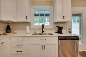 A modern kitchen with white cabinetry, a stainless steel sink, a coffee maker, and a dishwasher. - Walk to Lake & Paris Landing State Park! Quiet Gem (Buchanan)