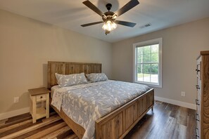 A bedroom with a wooden bed, a nightstand, a ceiling fan, and a window with a view of trees. - Walk to Lake & Paris Landing State Park! Quiet Gem (Buchanan)