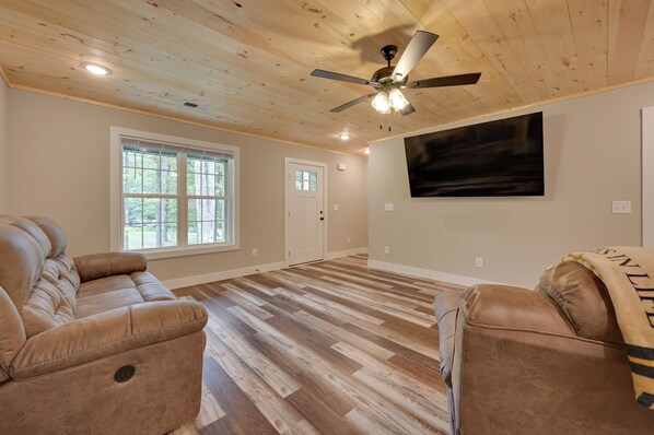A spacious room with a ceiling fan, large windows, a flat-screen TV, and leather sofas. - Walk to Lake & Paris Landing State Park! Quiet Gem (Buchanan)