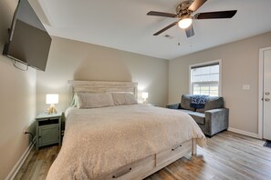 Une chambre à coucher avec un lit, une chaise, un ventilateur de plafond, une télévision et une fenêtre.