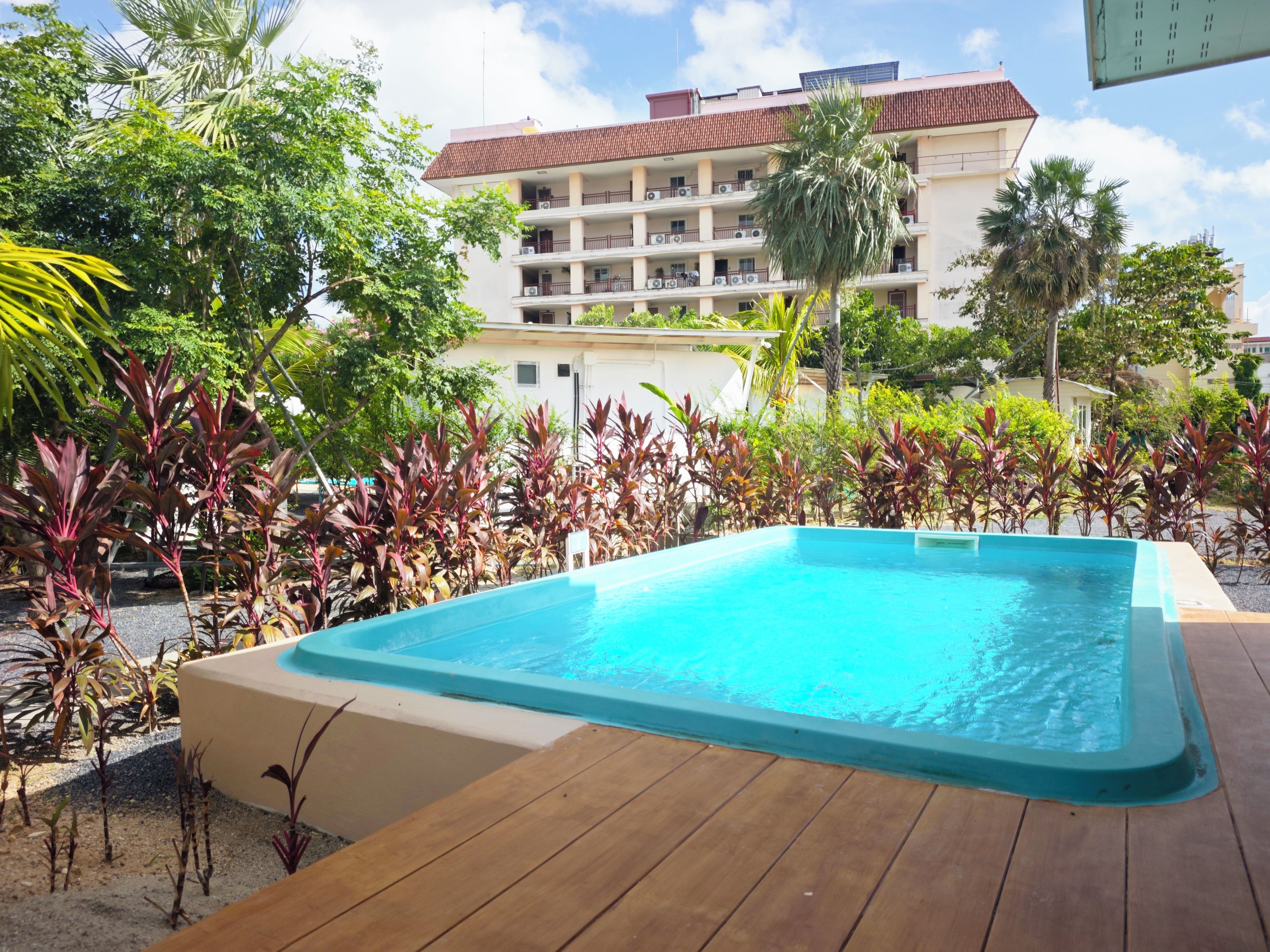 Una piscina rodeada de plantas tropicales y un edificio de varios pisos al fondo.