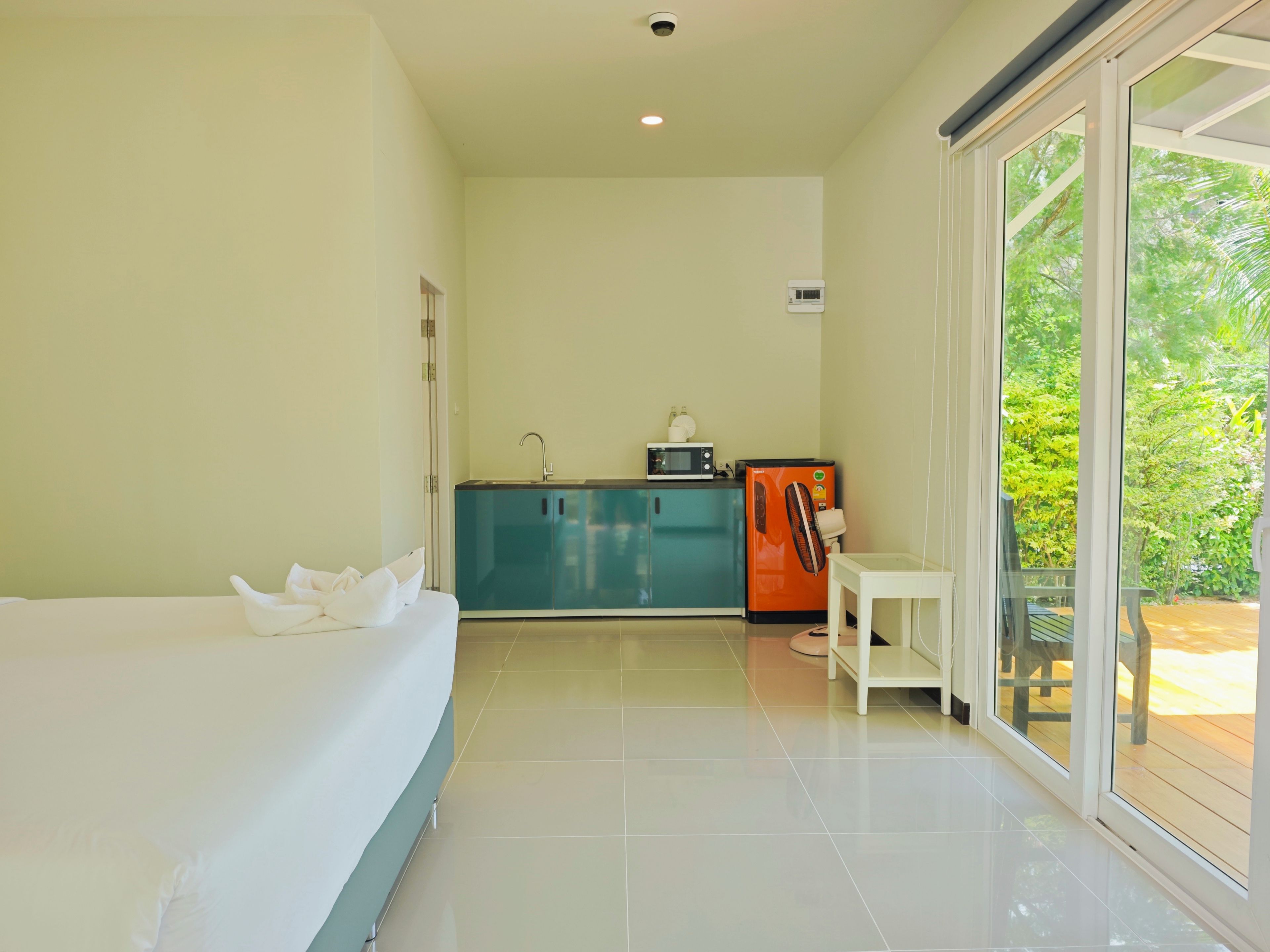 Habitación de hotel con cama, kitchenette y puerta corrediza de vidrio que da a un área exterior.