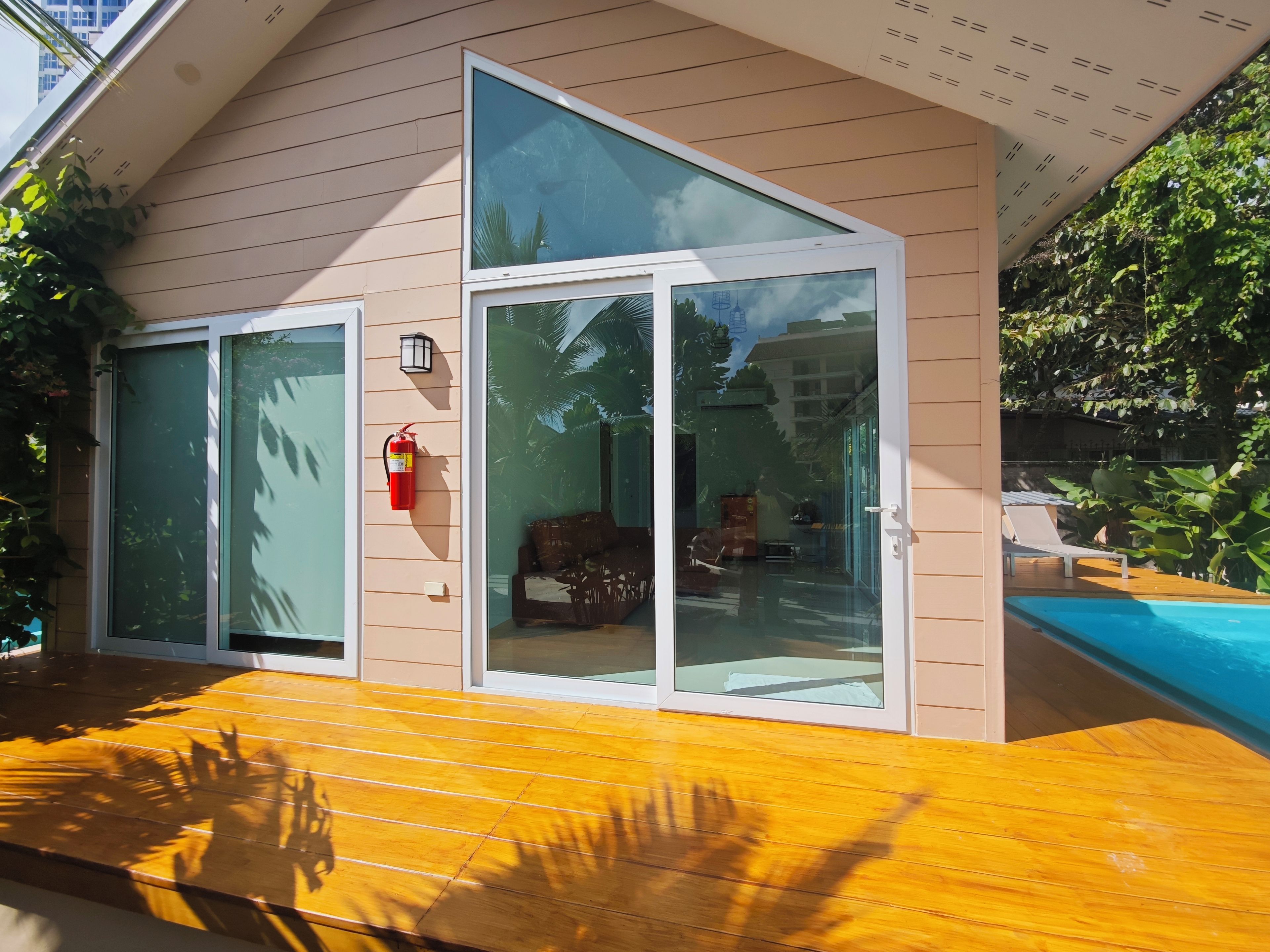 A modern house with a wooden deck, large glass doors, and a visible swimming pool.