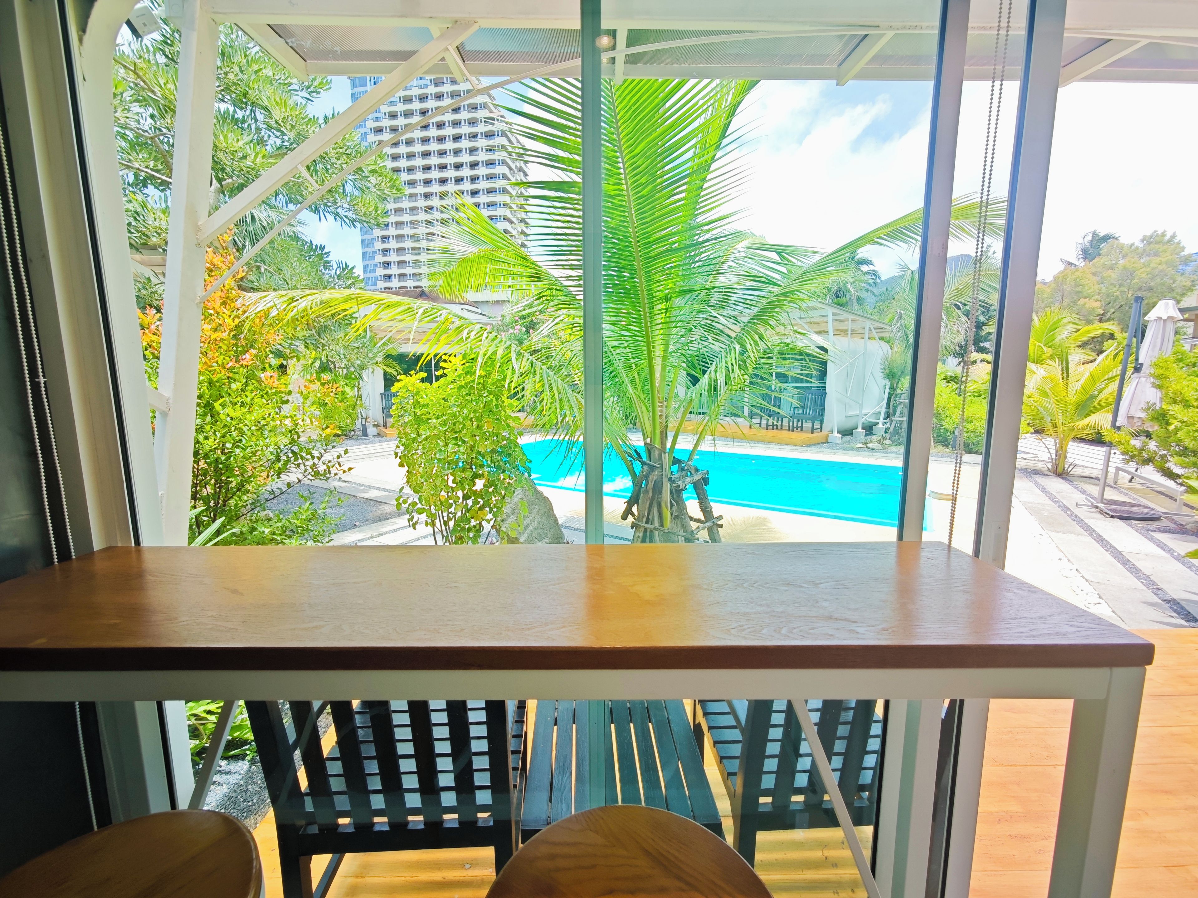 A room with a view of a swimming pool, surrounded by greenery and a tall building.