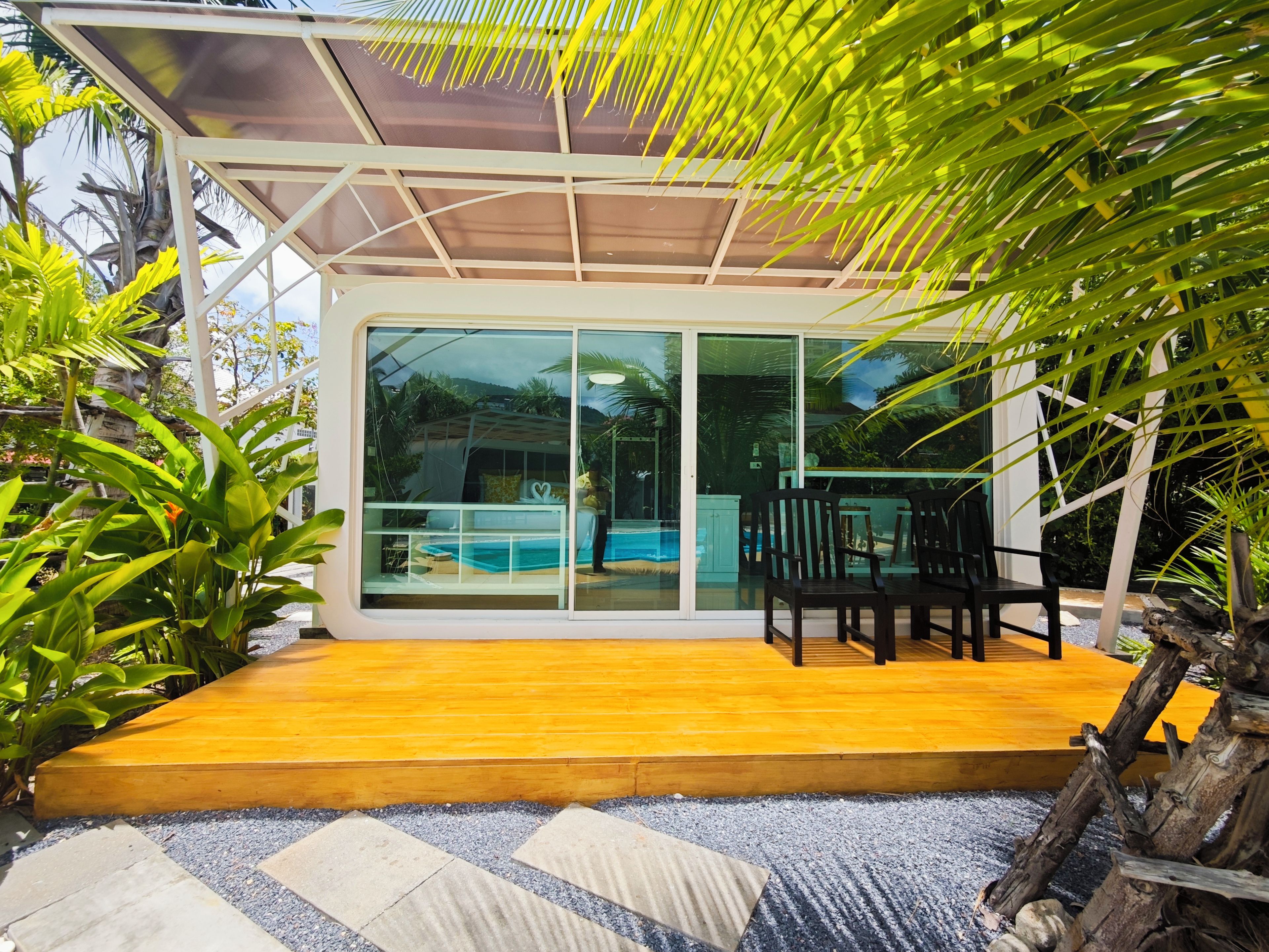 A modern house with a glass door leading to a pool area, surrounded by lush greenery.