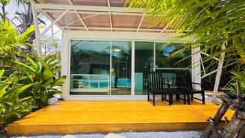 A modern house with a glass door leading to a pool area, surrounded by lush greenery.