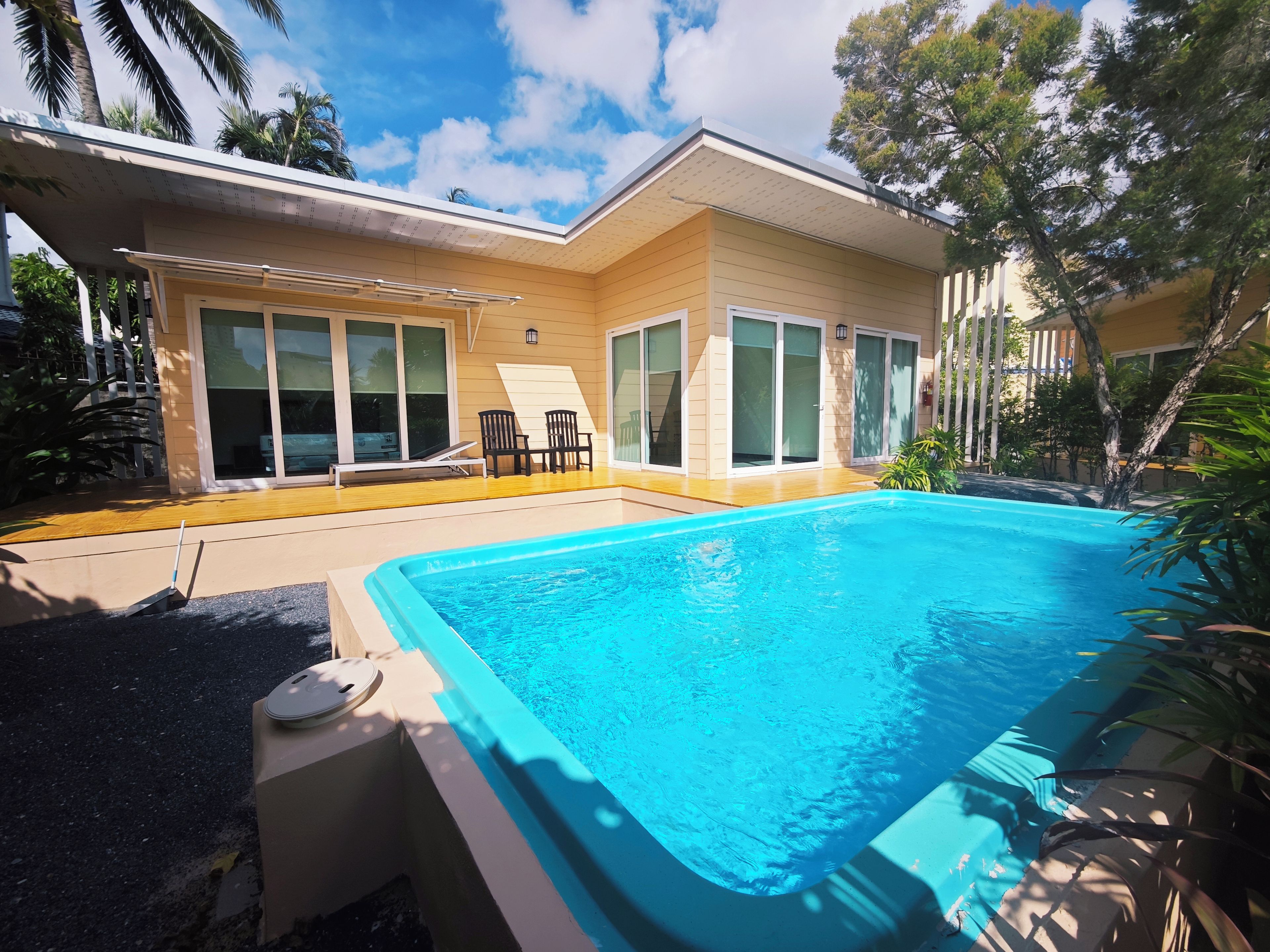 Una propiedad residencial con piscina, un patio cubierto con sillas y un amplio ventanal corredero.