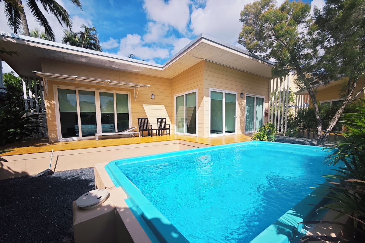 Una propiedad residencial con piscina, un patio cubierto con sillas y un amplio ventanal corredero.