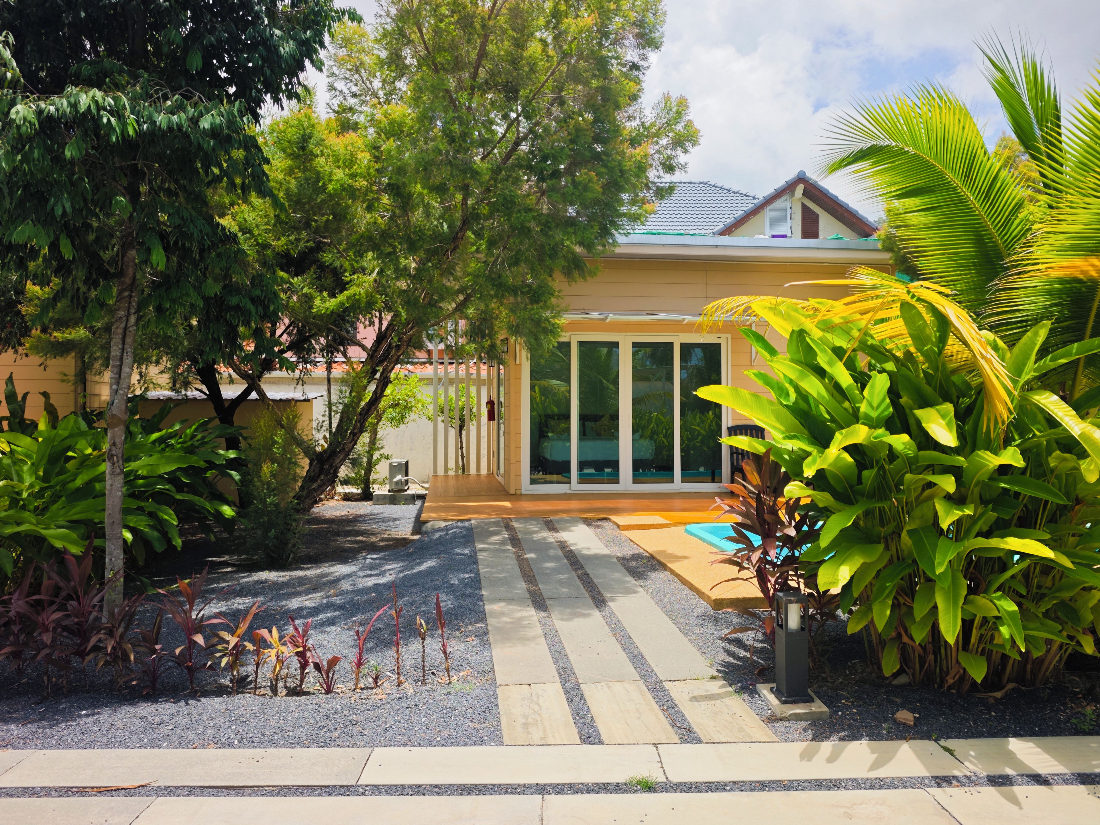 Una propiedad residencial con un patio cubierto, piscina y diversas plantas tropicales.