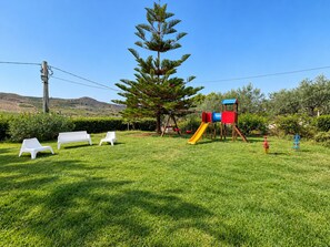 A grassy outdoor area with a playground featuring a slide and swings. - Vacation Home in Mazzarino with 1 bedrooms sleeps 2 (Mazzarino)