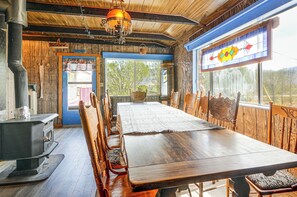 Ein rustikaler Essbereich aus Holz mit einem großen Tisch, Stühlen, einem Holzofen und einem Buntglasfenster.