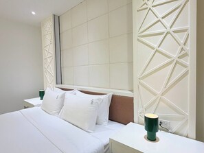 Ein Hotelzimmer mit einem großen Bett, weißer Bettwäsche, einem Kopfteil mit geometrischen Mustern, einem Nachttisch mit einer grünen Lampe und einer Wandverkleidung in ähnlichem Design.