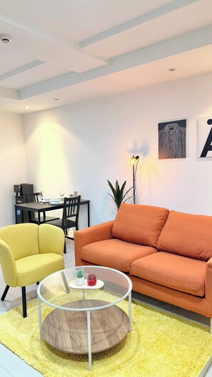 Ein modernes Wohnzimmer mit einer Couch, einem gelben Sessel, einem Glastisch und einem Essbereich mit Tisch und Stühlen.