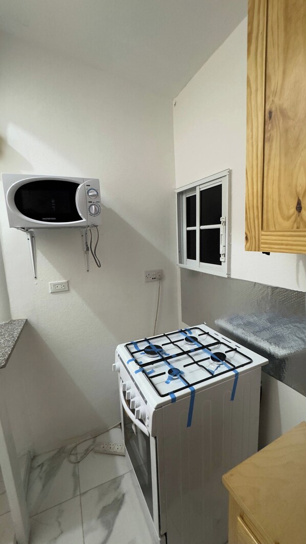 Une cuisine compacte équipée d’un four à micro-ondes encastré, d’une petite fenêtre et d’une cuisinière à gaz.