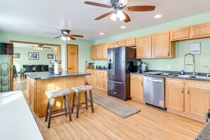 A modern kitchen with wooden cabinets, a stainless steel refrigerator, a dishwasher, and a bar area with stools. - 'WillowField' Fire Pits, Game Room & Group Fun (Roosevelt)