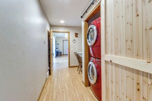 A laundry room with two stacked washing machines, wooden flooring, and a door leading to another room.