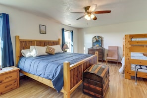 A wooden bed with a headboard, a bedside table, a dresser, a mirror, a chair, a ceiling fan, and a trunk.