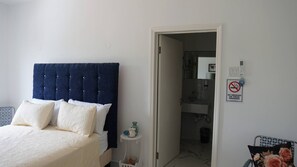 A bedroom with a bed, a bedside table, a nightstand, a door to a bathroom, and a no-smoking sign on the wall.