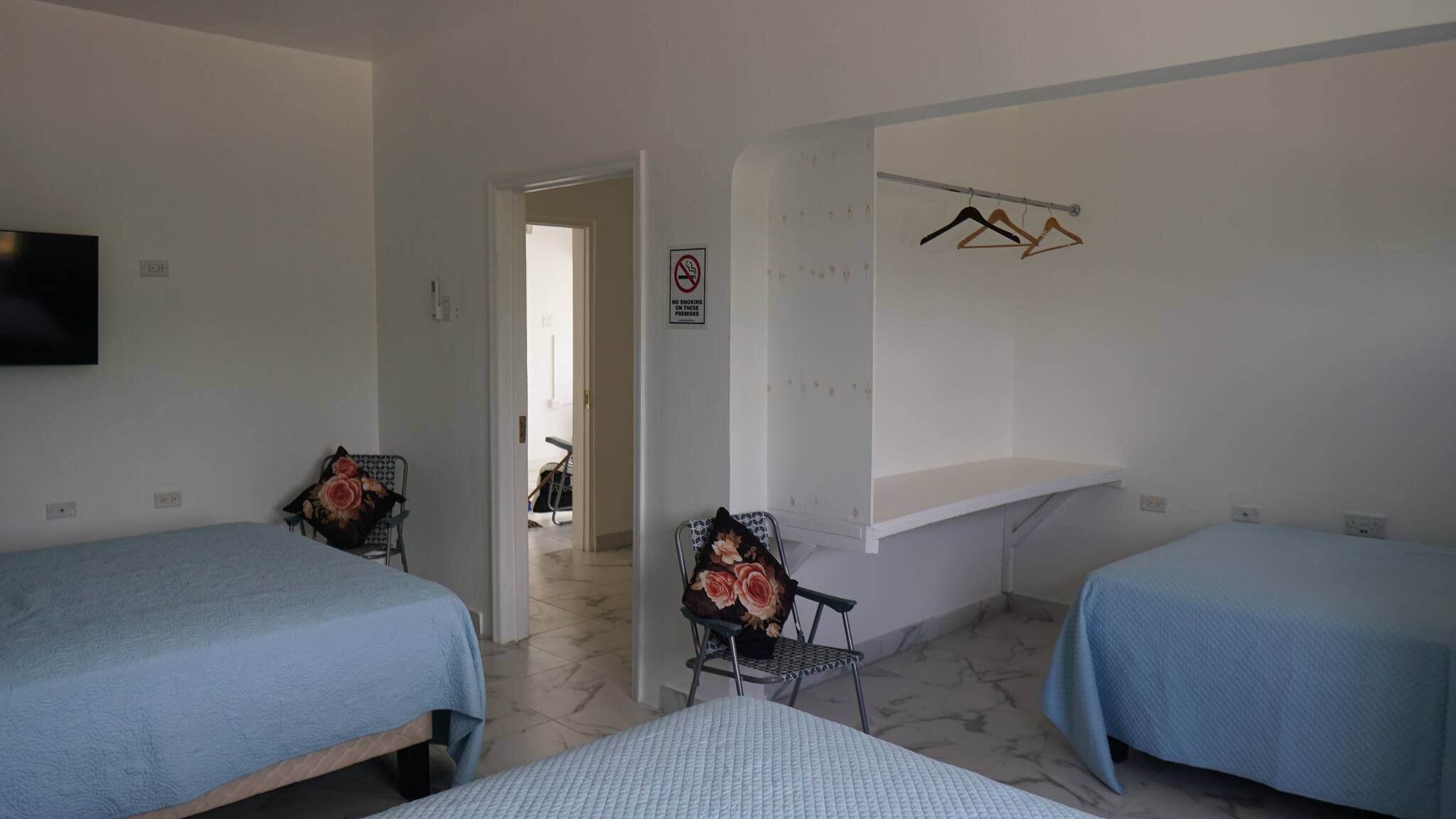 Ein Hotelzimmer mit zwei Betten, einem Fernseher, einem Sessel mit Blumenkissen, einem Rauchverbotsschild und einem Kleiderhaken.