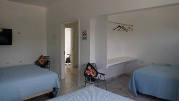 Ein Hotelzimmer mit zwei Betten, einem Fernseher, einem Sessel mit Blumenkissen, einem Rauchverbotsschild und einem Kleiderhaken.