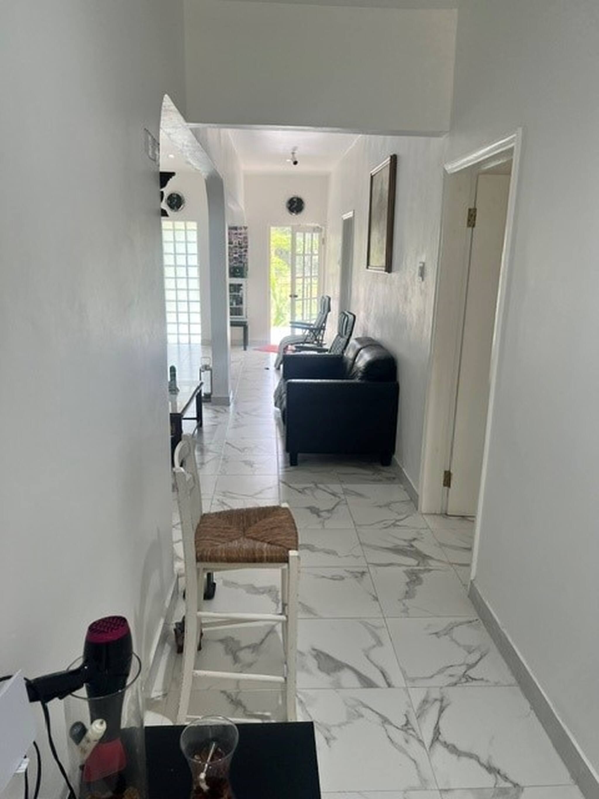 Um corredor com uma cadeira branca, um sofá preto e piso de mármore.