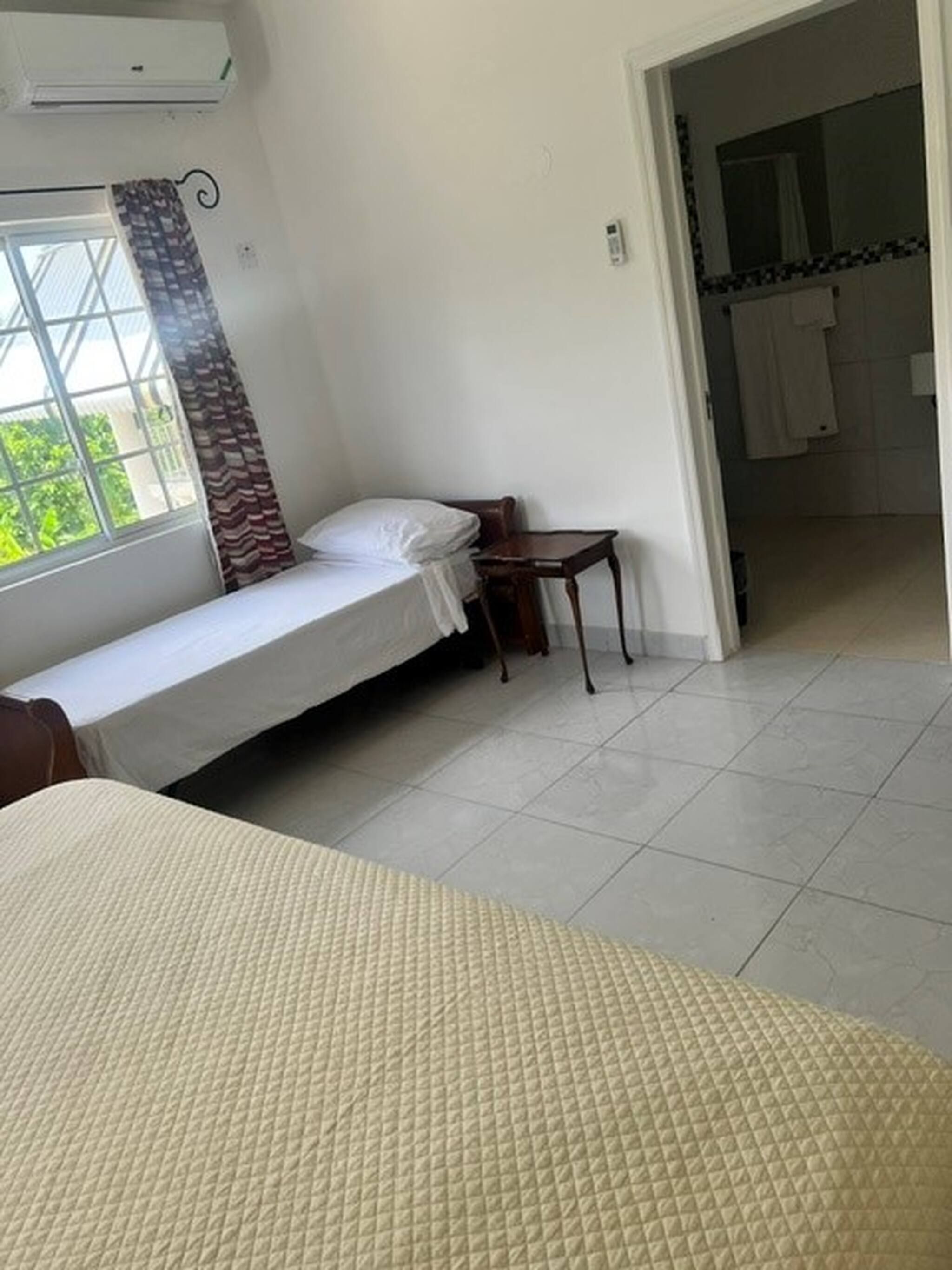 Een kamer met een enkel bed, een tafeltje en een raam met gordijnen.
