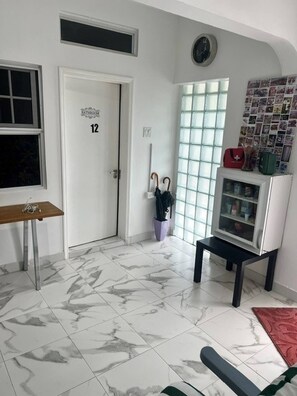 A hotel room with a marble floor, a wooden table, a door labeled '12', a glass cabinet, and a wall with a grid of photos.