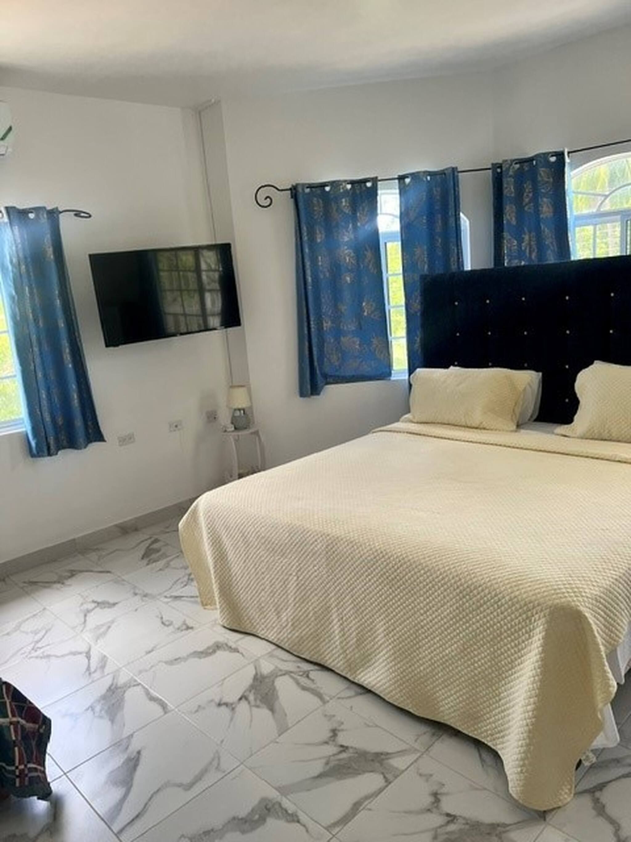 Quarto com cama, televisão de tela plana, mesa de cabeceira e janela com cortinas.
