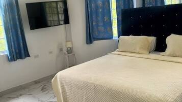 Quarto com cama, televisão de tela plana, mesa de cabeceira e janela com cortinas.