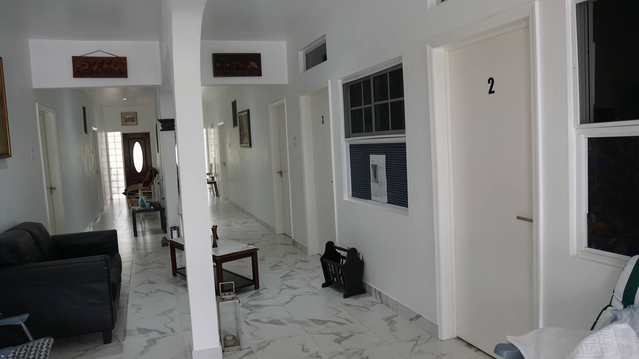 Um corredor com chão de mármore, um sofá preto, uma mesinha e uma porta com o número 2.