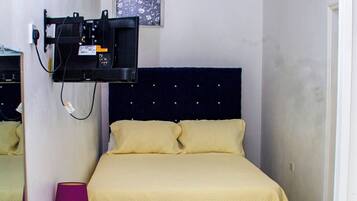 Une chambre à coucher comprenant un lit, un ventilateur de plafond, un téléviseur fixé au mur, une petite table avec une lampe et une chaise.