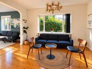 A living room with a dark blue sofa, two wooden chairs, a round coffee table, and a large window with a view of greenery. - Charming Private Apartment in the Heart of København (København)