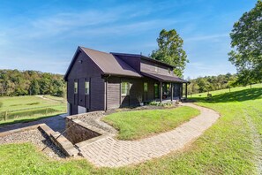 Une cabane en rondins avec un toit en pente, une véranda et un chemin en briques menant à l’entrée.