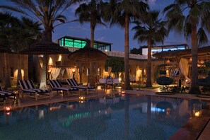 Un área de piscina con sillones de descanso, sombrillas y un edificio con una ventana iluminada.