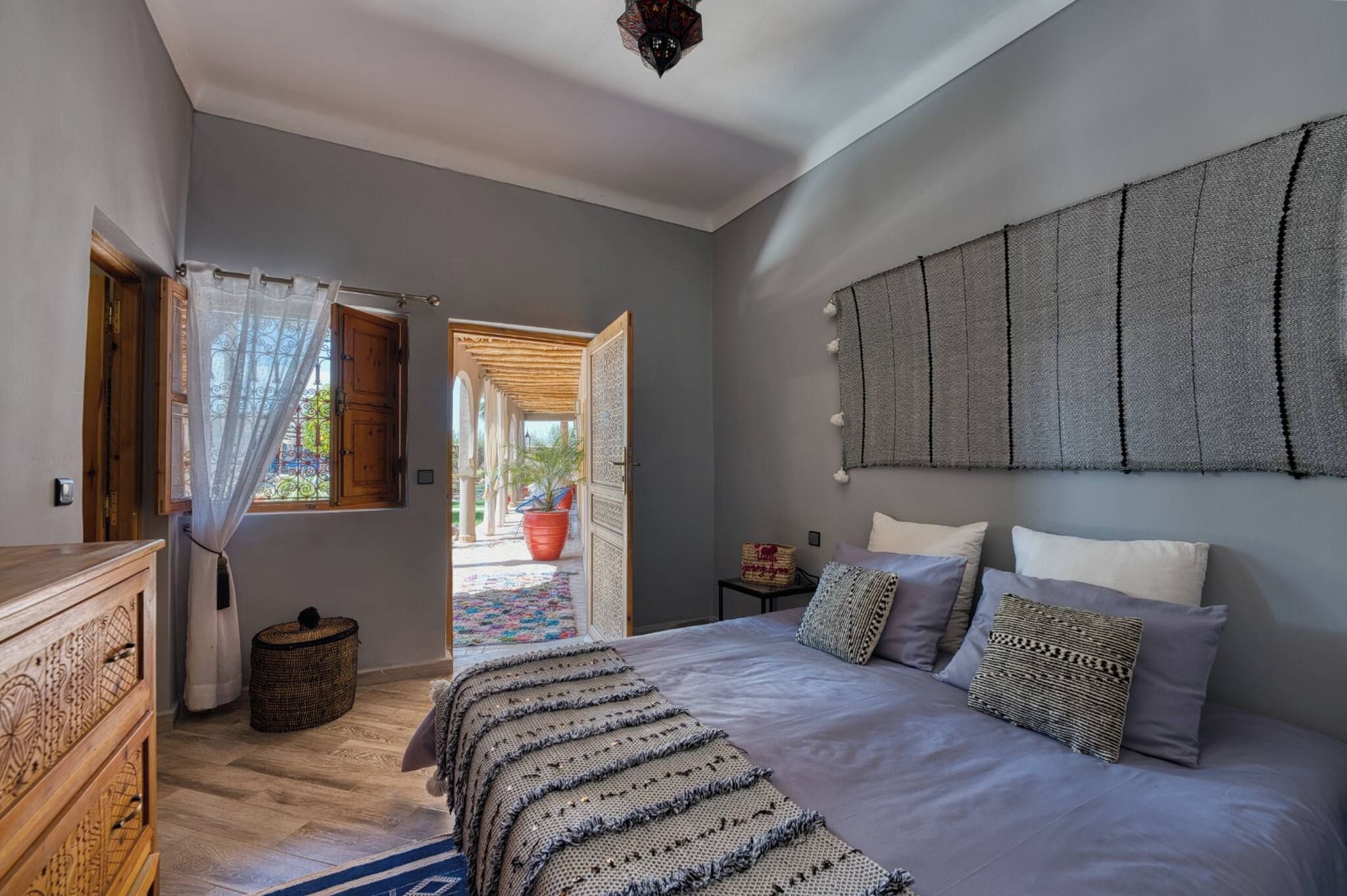 Une chambre avec un grand lit, une commode en bois, une fenêtre avec des rideaux et une vue sur l’extérieur.