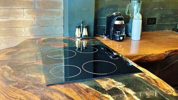 A kitchen with a wooden countertop, a black induction cooktop, a blender, and a coffee maker.