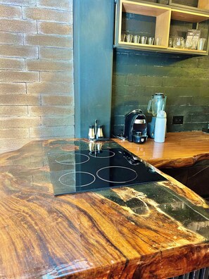 Eine Küche mit einer Holzausziehtafel, einem schwarzen Induktionskochfeld, einem Mixer und einer Kaffeemaschine.