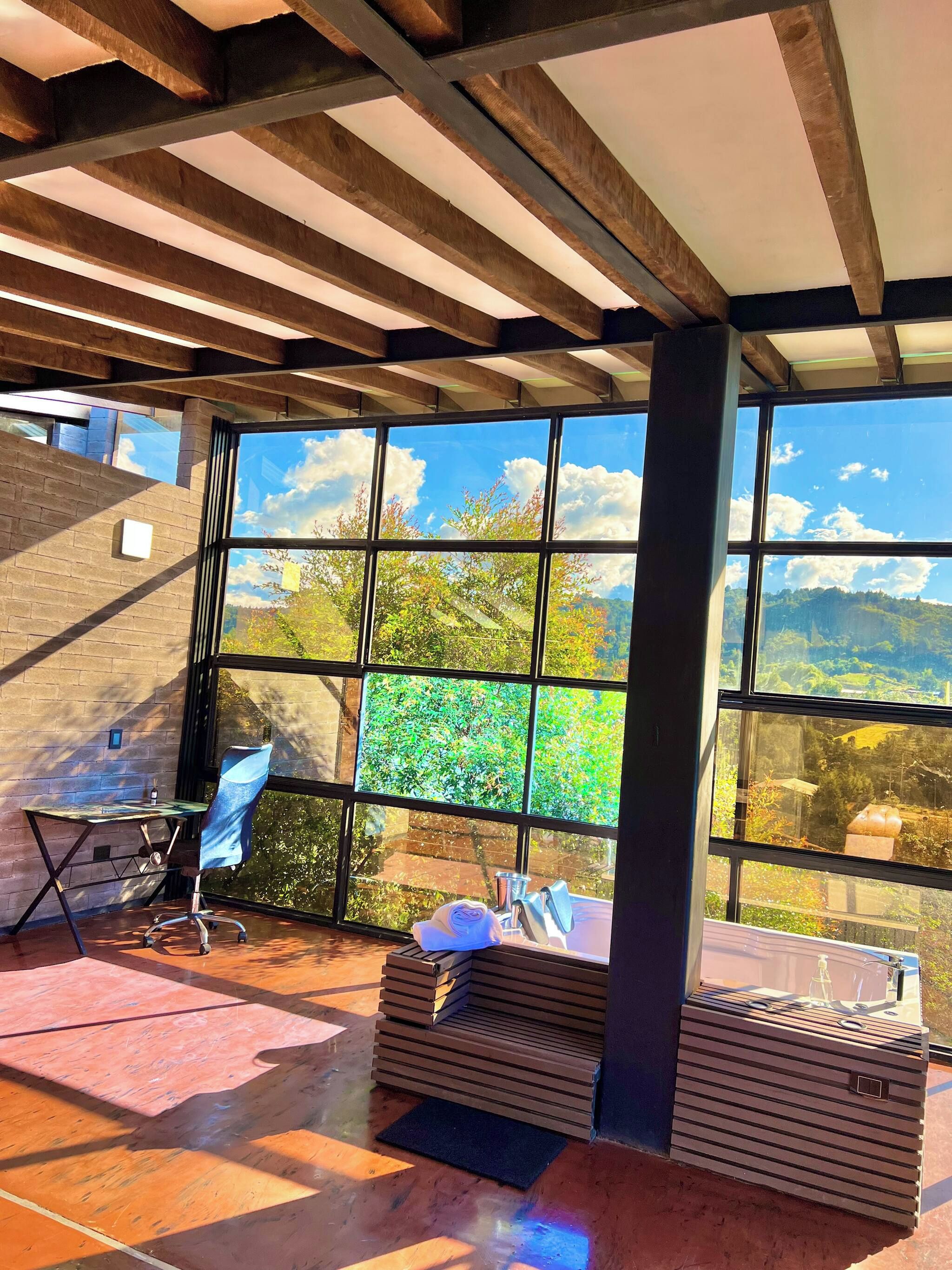 Une pièce avec une grande fenêtre, une chaise, un bureau et une pile de planches de bois.