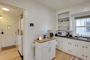 A modern kitchen with white cabinetry, a coffee machine, a microwave, and a window with blinds. - Stroll to Olde Town Arvada! Charming Gem (Arvada)