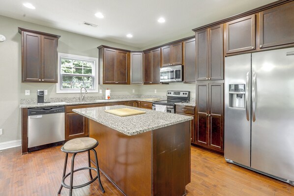 A kitchen with wooden cabinets, stainless steel appliances, a granite countertop, and a window.