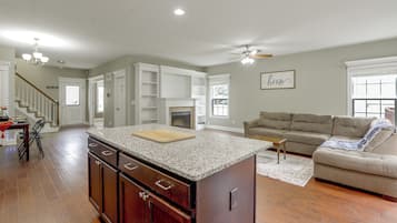 A spacious living area with a kitchen island, a fireplace, and a staircase leading to an upper level.