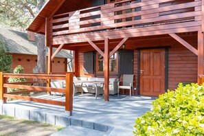 A wooden cabin with a covered patio, outdoor seating, and a wooden fence. - Holiday home with 2 bedrooms (Dzwirzyno)