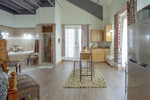 Una cocina moderna con refrigerador, armarios de madera, un comedor con mesa y sillas, y un baño con bañera y ducha.